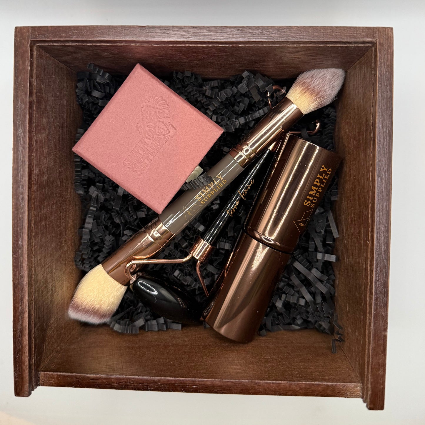 Set of beauty tools including a roller, brush, and pink bar in a wooden box.