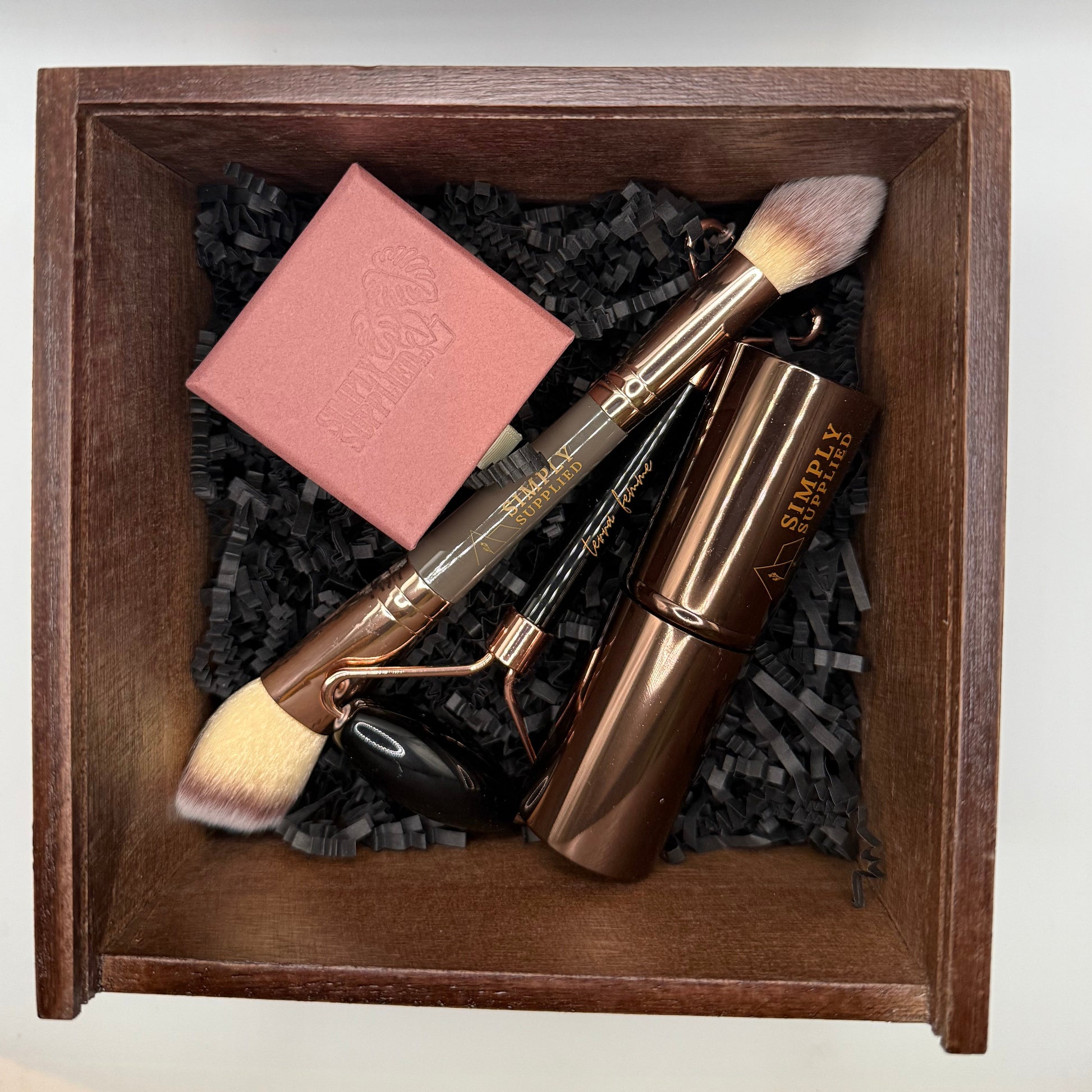 Set of beauty tools including a roller, brush, and pink bar in a wooden box.