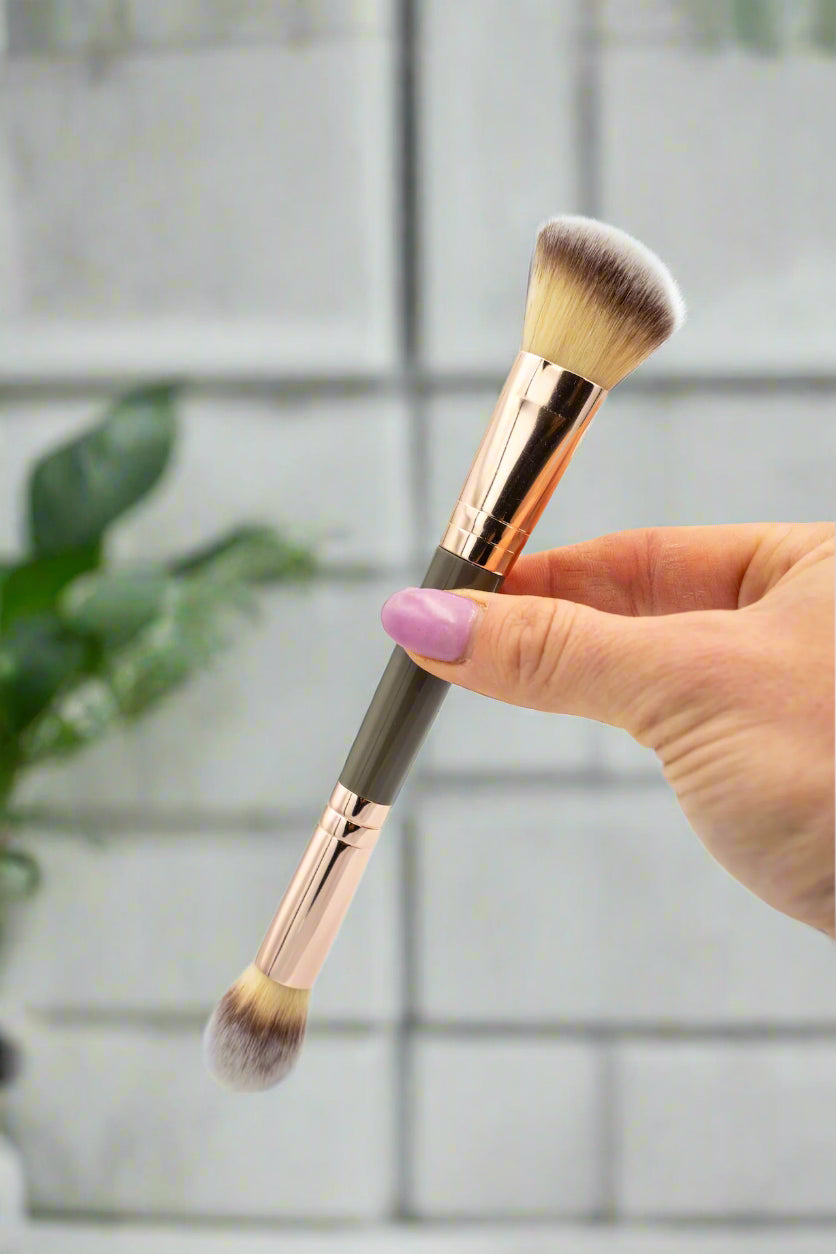 Makeup brush held by a hand with a light gray background