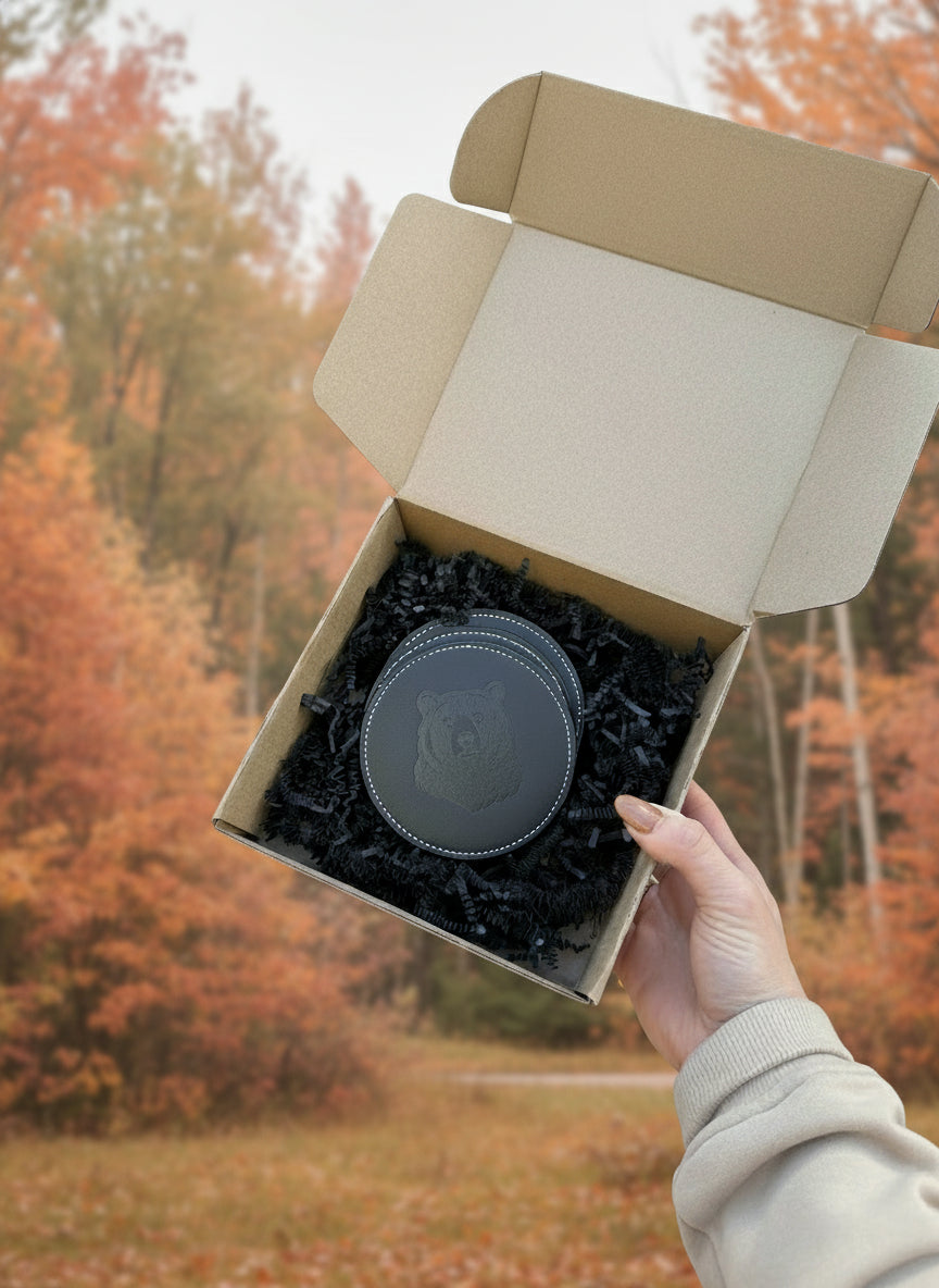 Round black leather item with bear design in a cardboard box held by a hand.