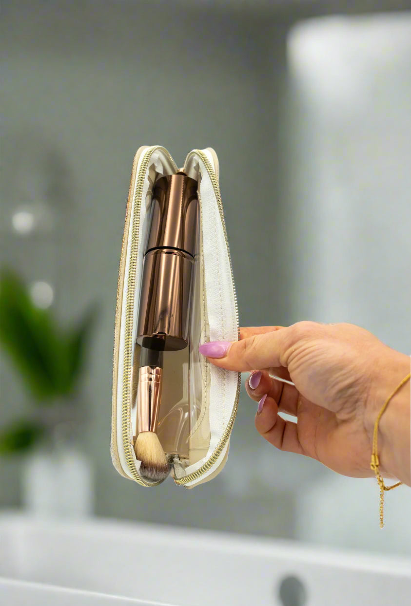 Hand holding a rose gold makeup brush set in a clear case against a white background