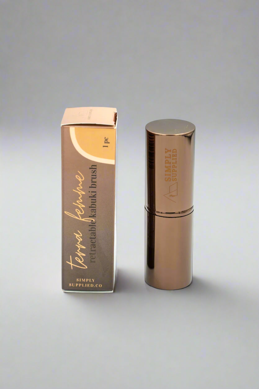 Bronze-colored makeup brush with packaging on a light gray background