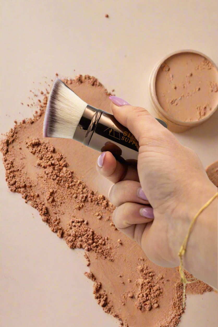 Hand holding a makeup brush with a visible brand name against a light background