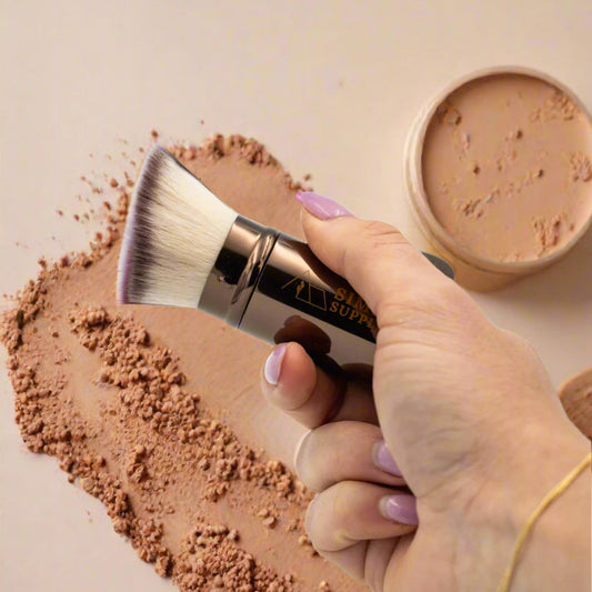 Hand holding a makeup brush with a visible brand name against a light background